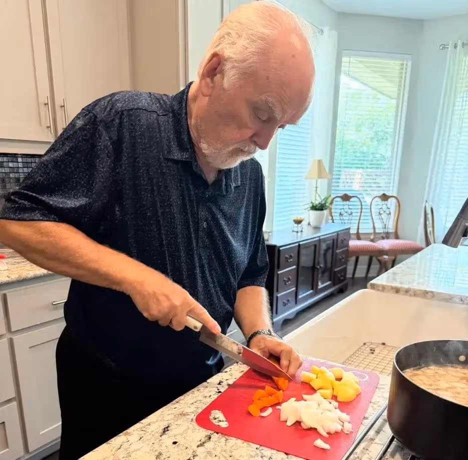 Alan preparing food in a bright kitchen, cutting vegetables on a countertop.