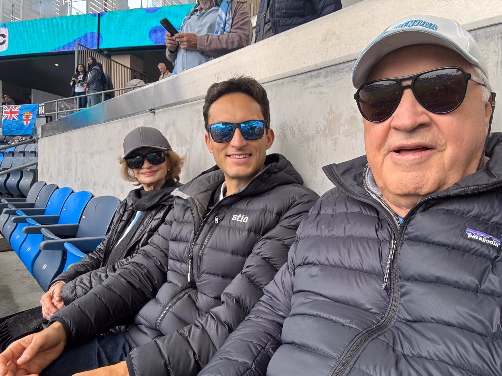 JP with family at a stadium, wearing jackets and sunglasses