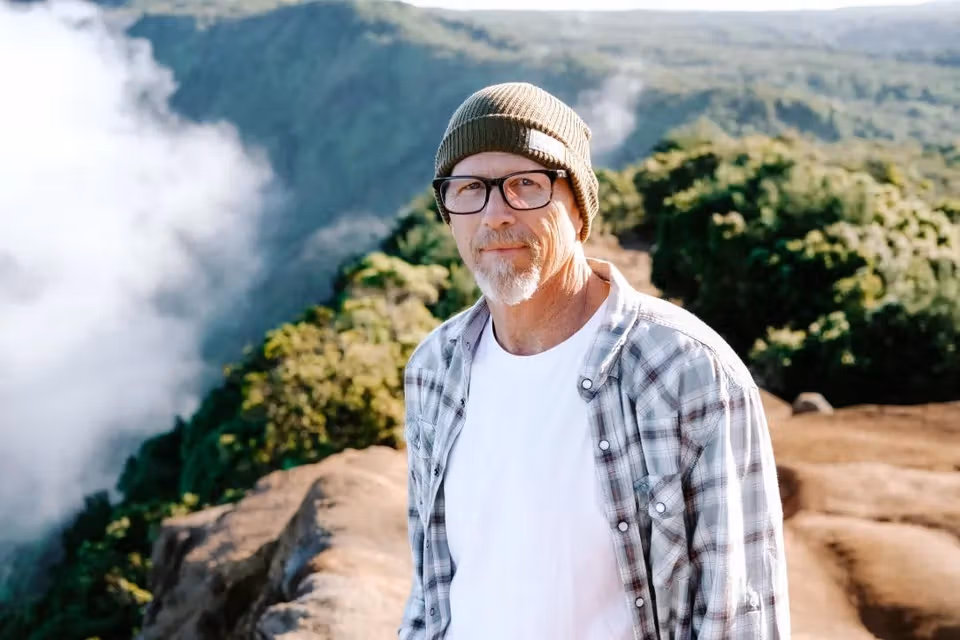 Alan standing outdoors near a scenic overlook, wearing a beanie and glasses.