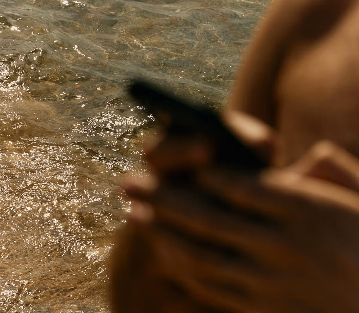Close-up of sparkling river water with a blurred figure in the foreground holding a phone