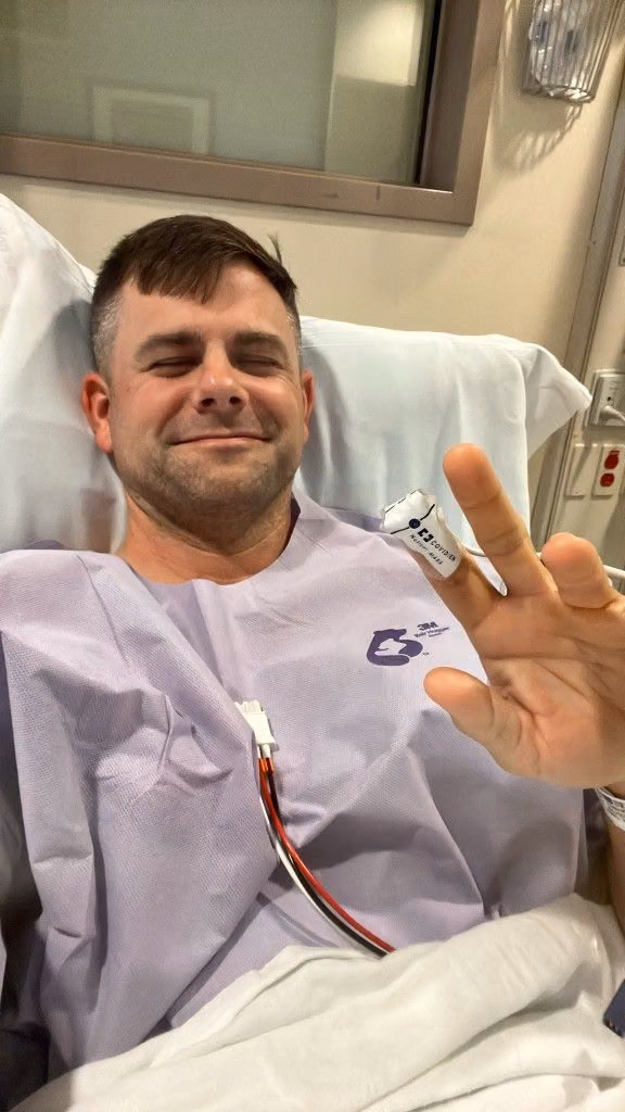 Tanner in a hospital gown after surgery, holding up a peace sign.