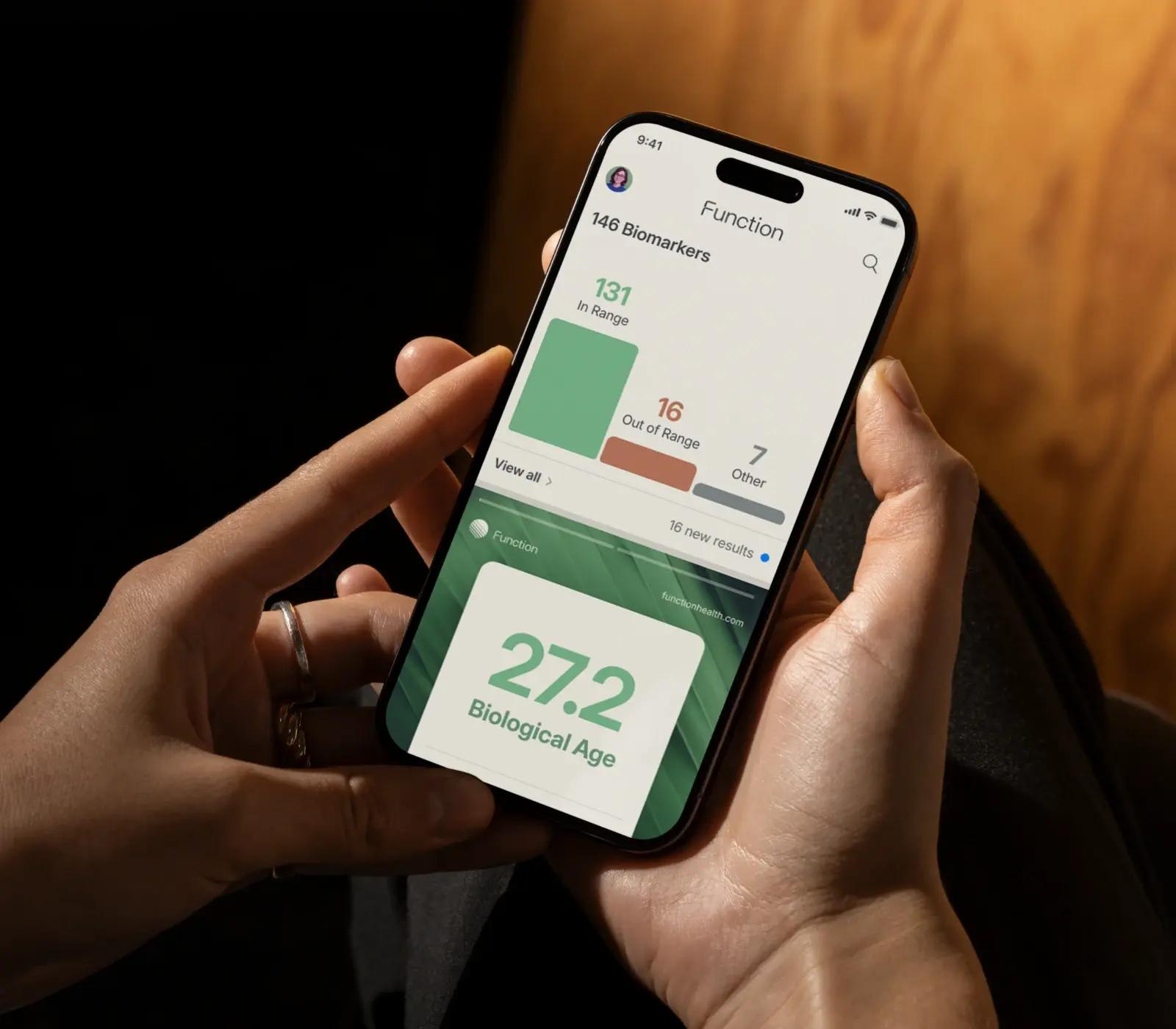 Person holding phone showcasing Function Health results with 100+ biomarkers and a biological age of 37.2.