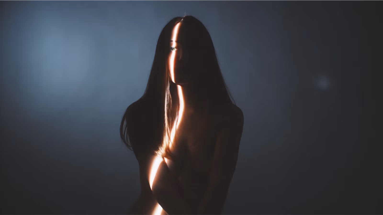 Silhouette of a person with long hair, lit by a narrow beam of light cutting vertically across their face and body against a dark, moody background