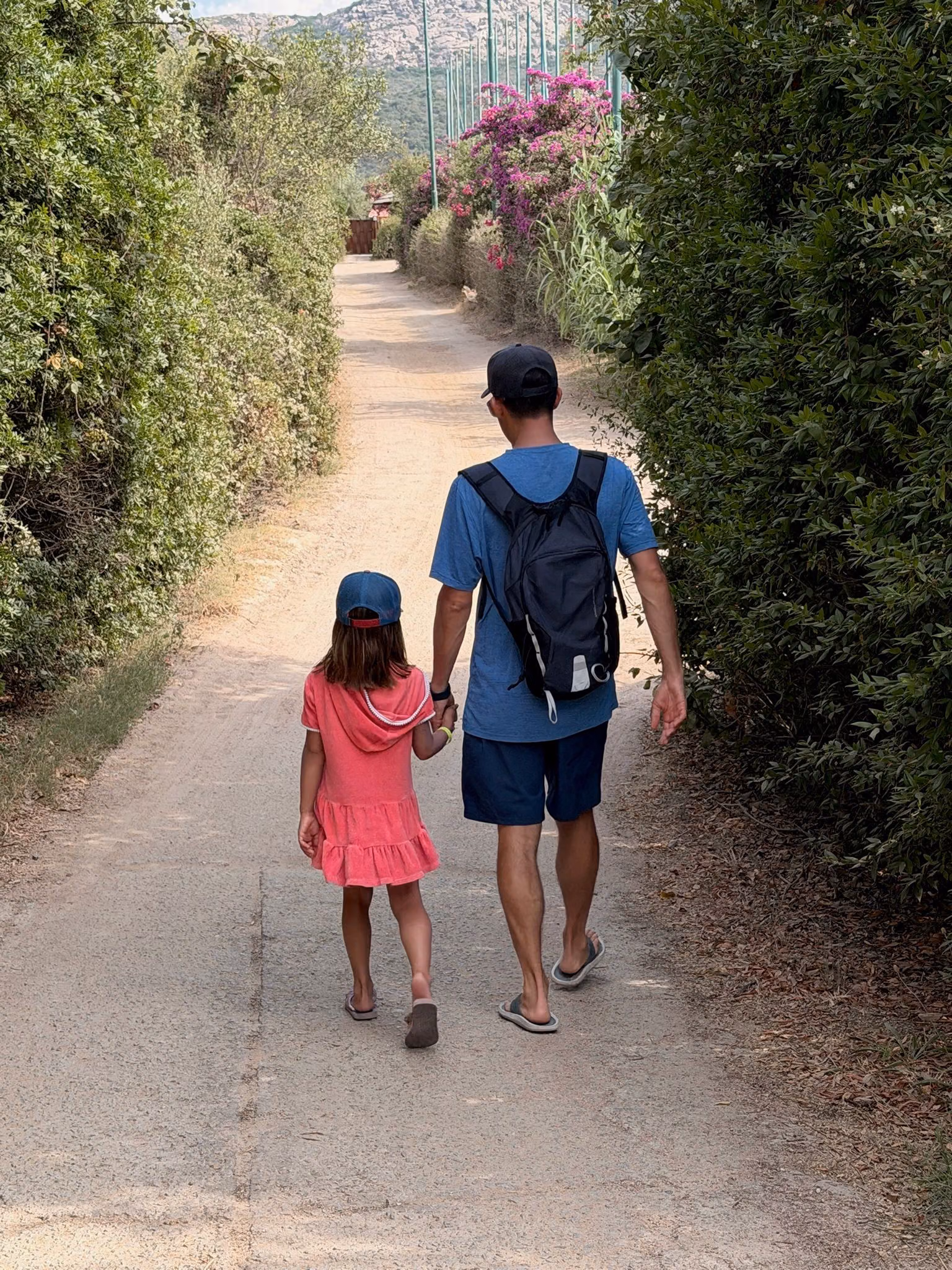 JP walking hand in hand with his daughter along a path lined with flowers
