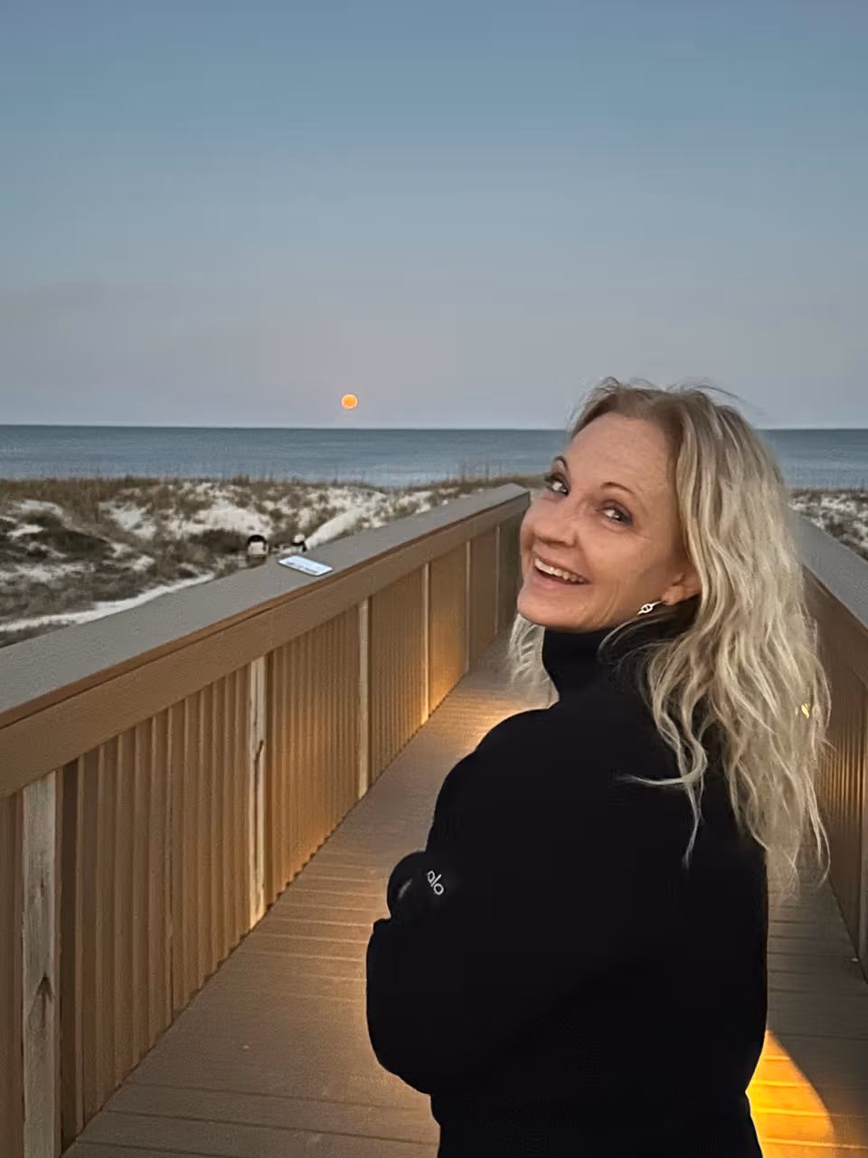 Cari smiling on a boardwalk at sunset with the beach and ocean behind her.