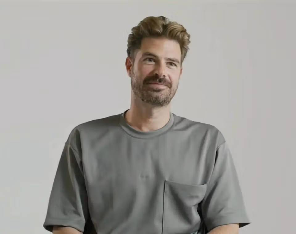 Geoff seated in a gray T-shirt against a light studio backdrop, smiling slightly.