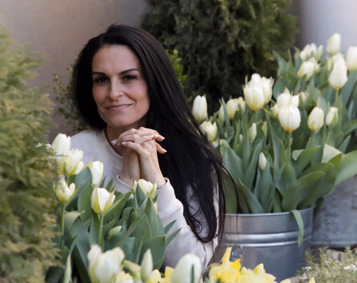 Melissa seated among white tulips outdoors with her hands clasped under her chin.