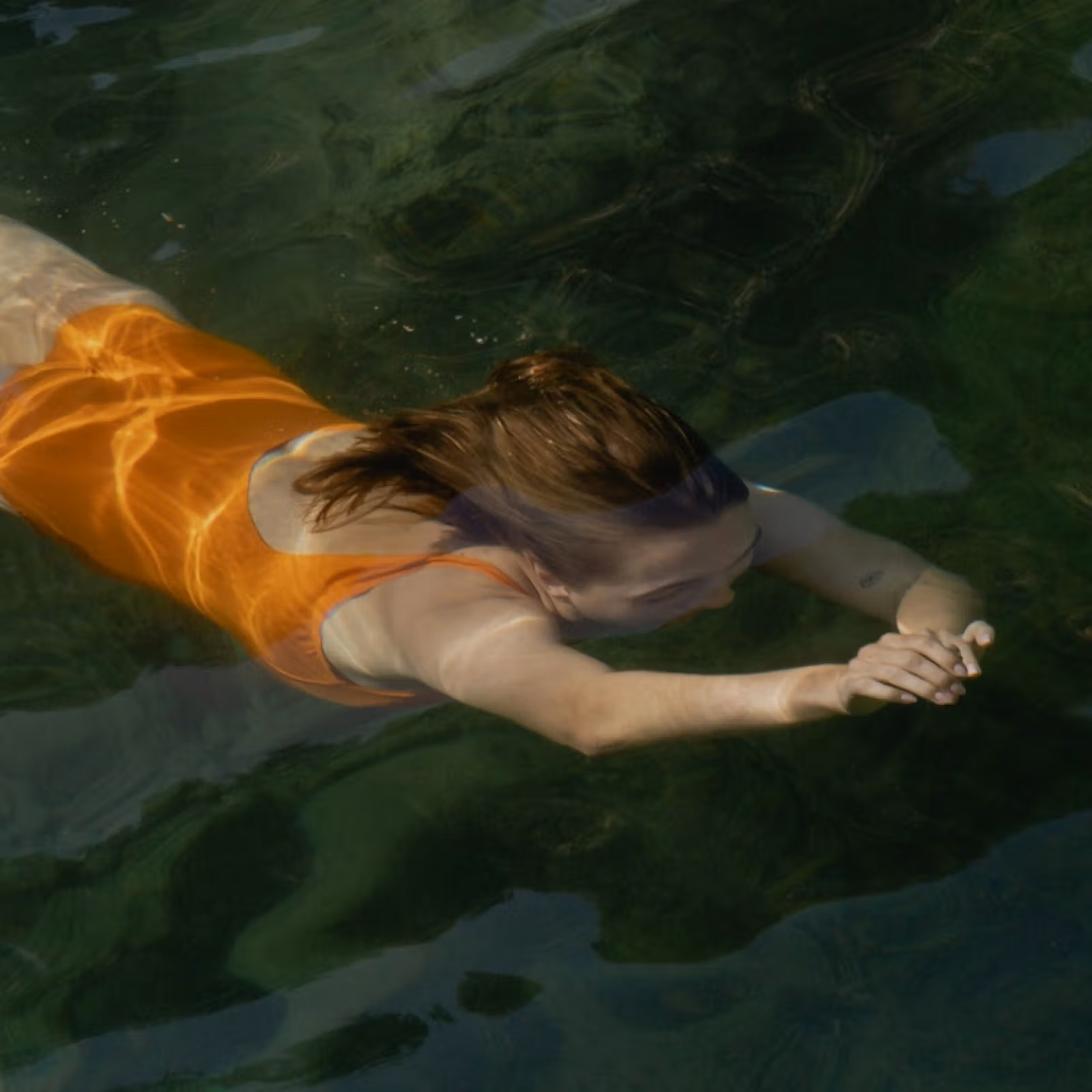 Person swimming underwater in an orange top with arms extended forward.