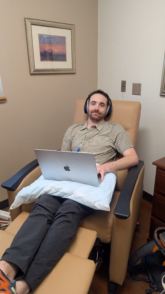Mitchell receiving chemotherapy while working on a laptop in a treatment chair.