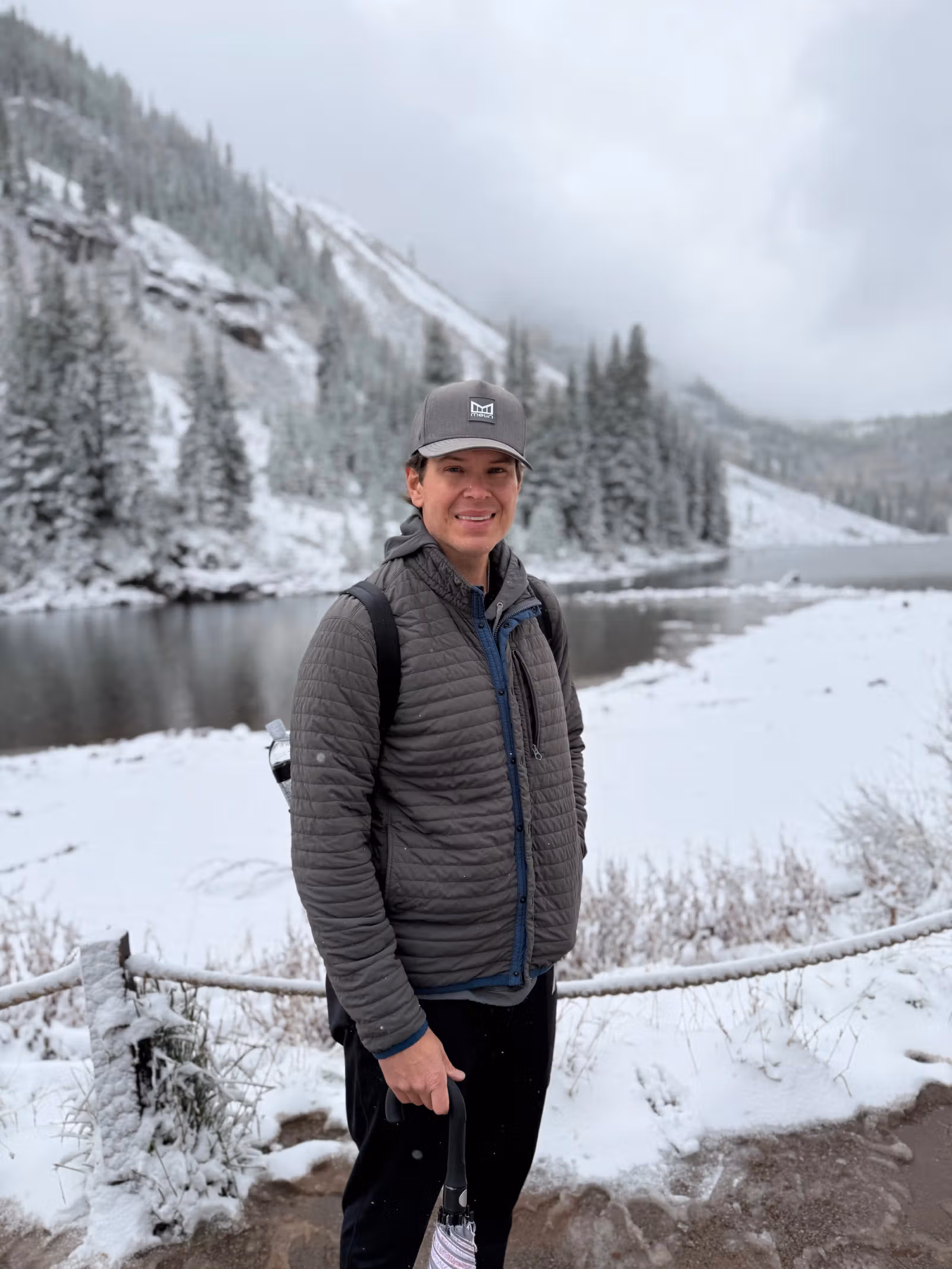 Travis standing in a snowy mountain landscape beside a river, smiling at the camera.
