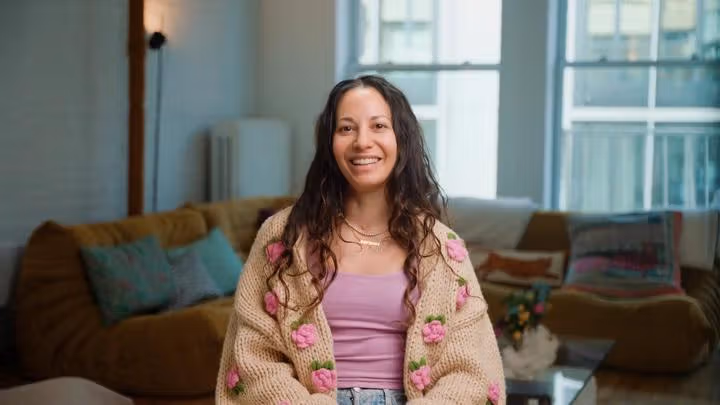 Aimee seated indoors on a sofa and smiling toward the camera.