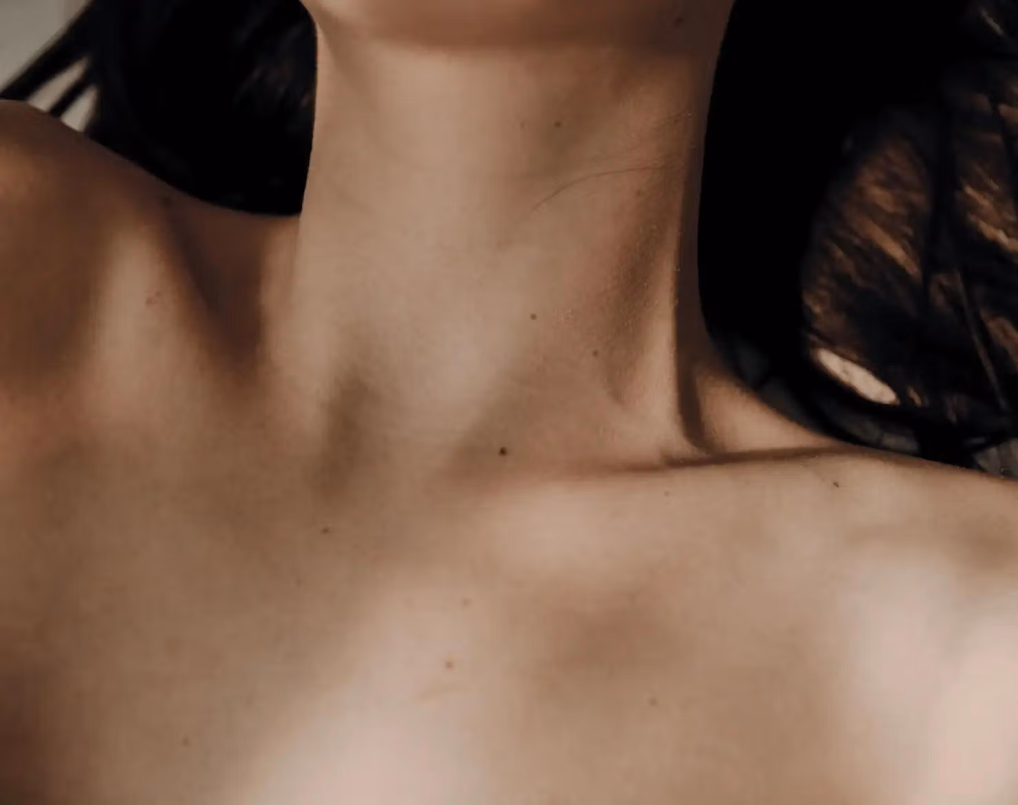 Close-up of a person's neck and collarbones against a dark background.